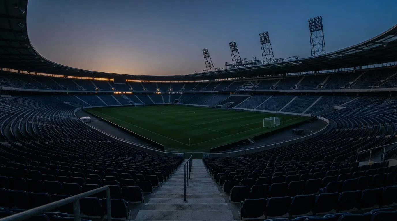 An empty football stadium with floodlight masts at dusk